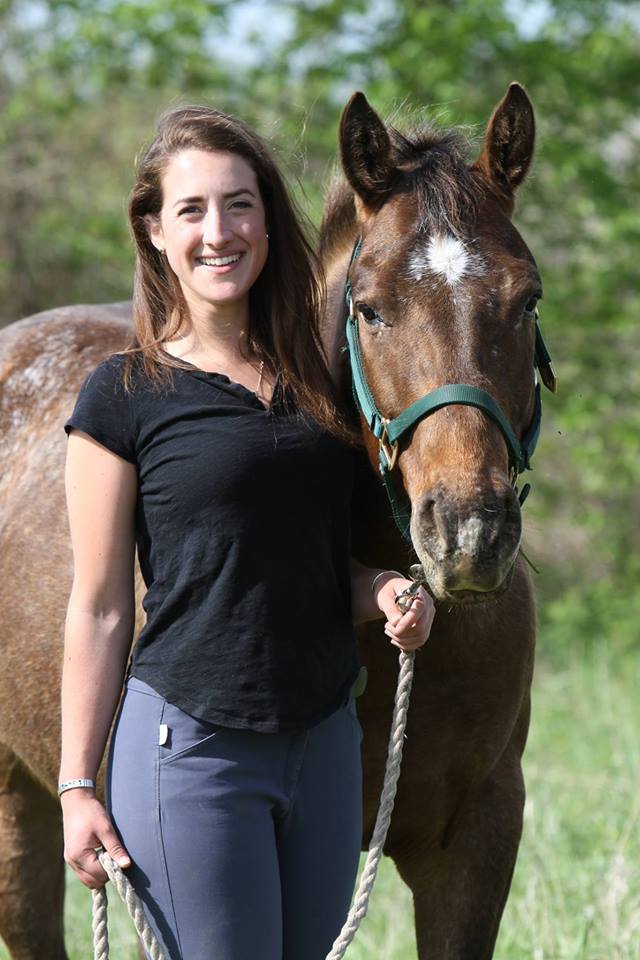 Dr. Devan Catalano of Woody's Feed posing in a green field, with her brown horse, Tio.