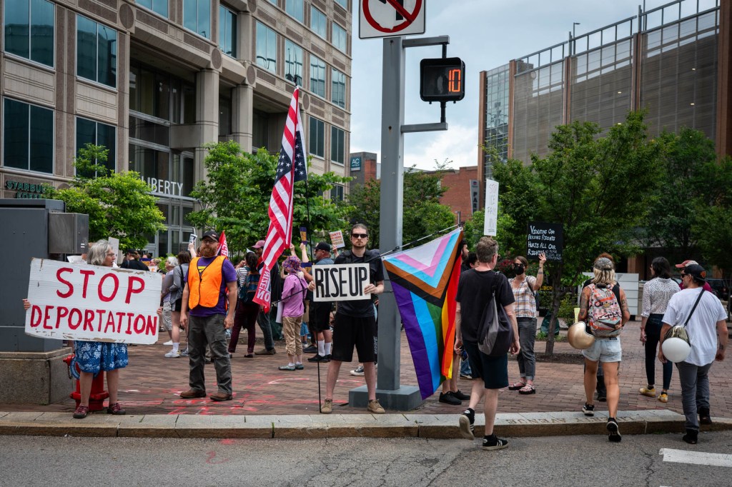 A group of people protest on a city street holding signs that read 