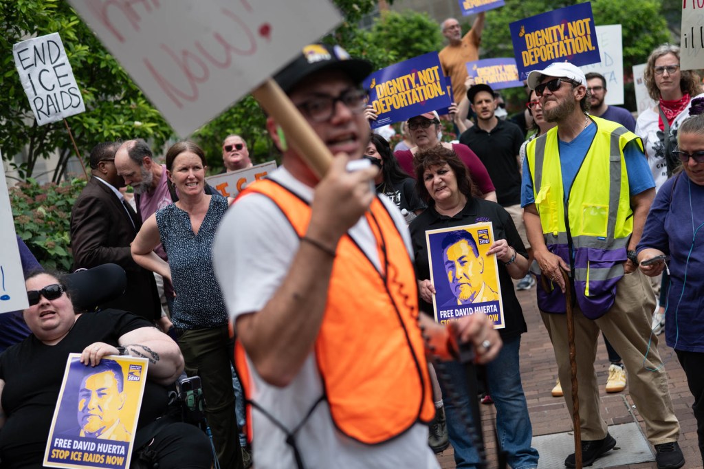 A group of people at a protest hold signs reading 